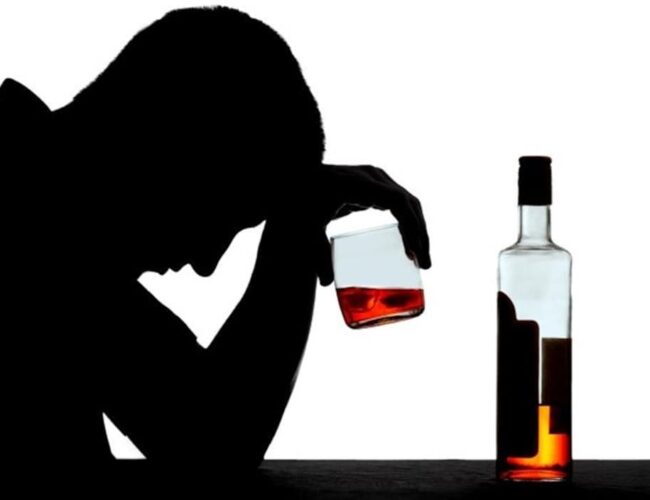 silhouette d'une personne alcoolique tenant un verre plein avec une bouteille posée sur une table